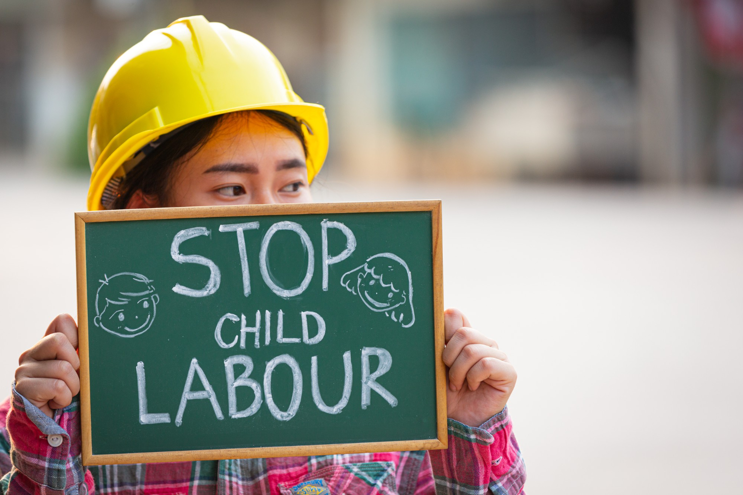 Girl in construction helmet holding a sign that says Stop Child Labor